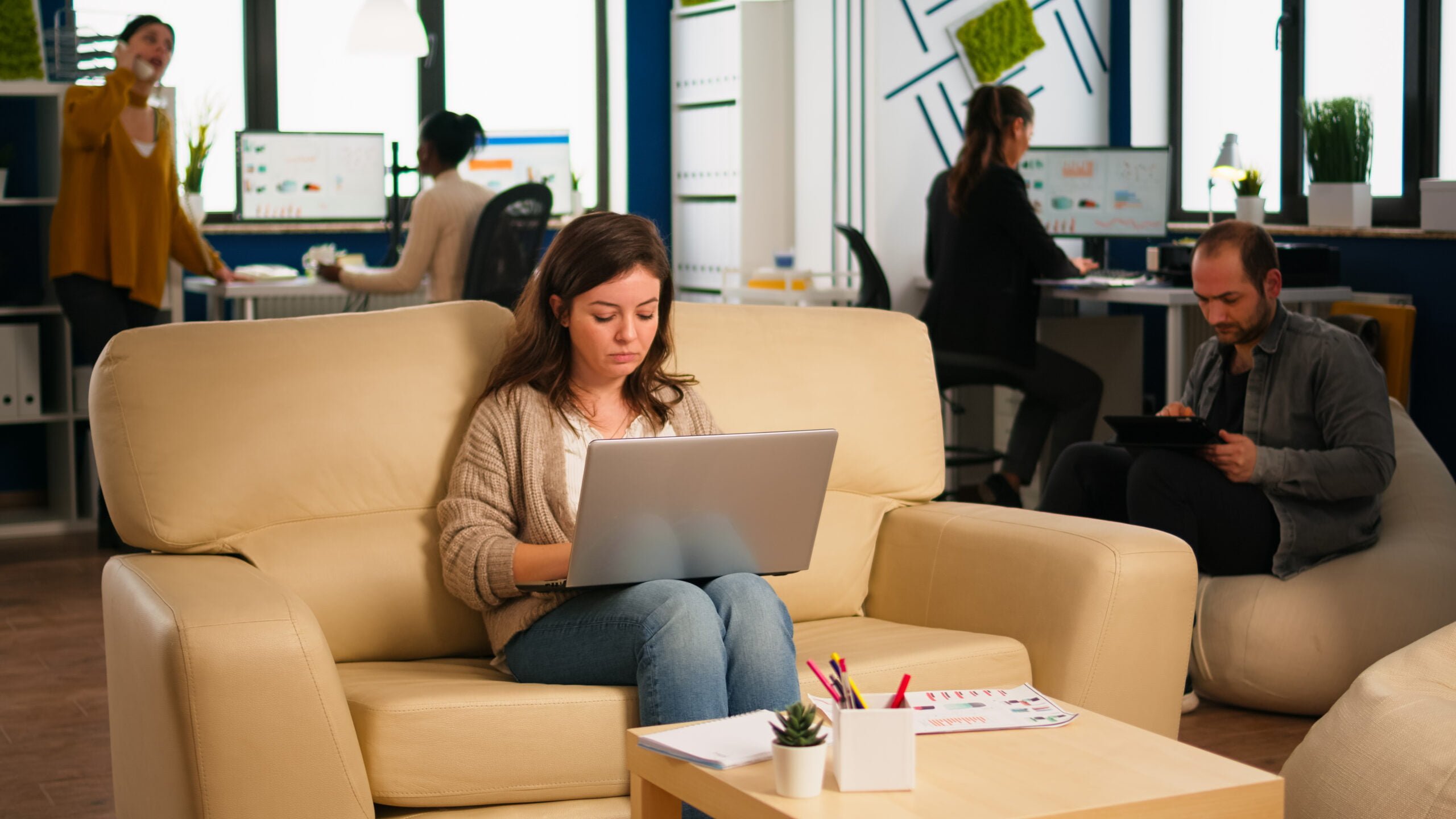 employee holding laptop sitting relax zone confortable couch typing pc smiling while diverse colleagues working background multiethnic coworkers planning new financial project company scaled