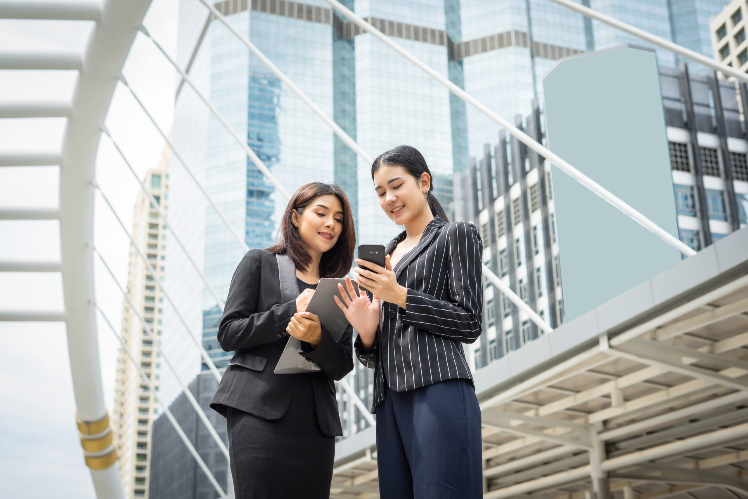 two business woman standing using smartphone discussing front office business working concept scaled two business woman standing using smartphone discussing front office business working concept scaled